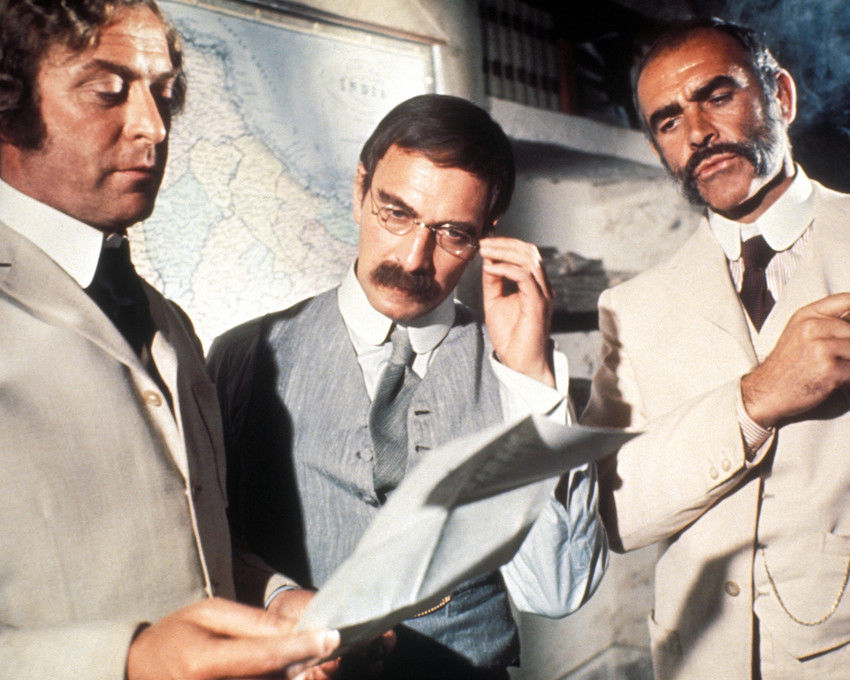 Tres hombres revisan un mapa y documentos en una escena de “El hombre que pudo reinar”.